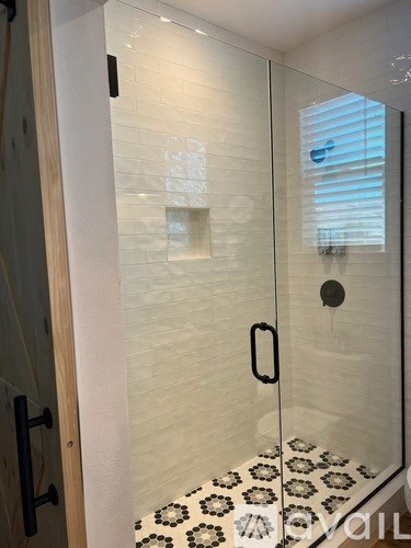 A white tiled shower with a glass door and a black handle.