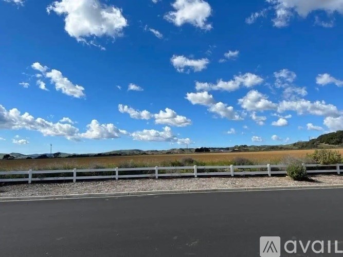 A road with a white fence and a cloudy sky in the background.