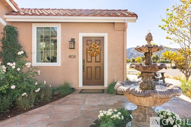 A house with a brown door and a stone pathway leading to a fountain.