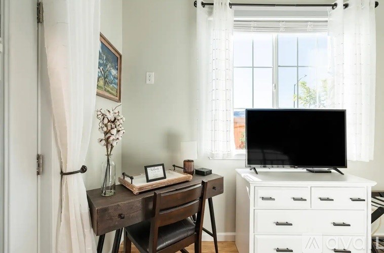 A room with a desk, chair, and a television.