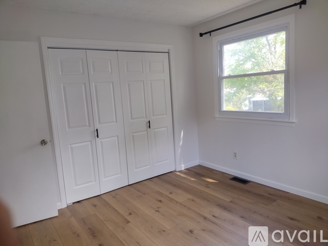 A room with a white door and a window with a view of trees outside.