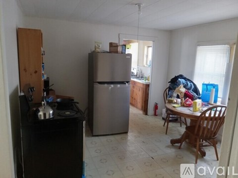 A kitchen with a black stove top oven, a wooden cabinet, a black fridge, a wooden dining table with chairs, and a window with blinds.