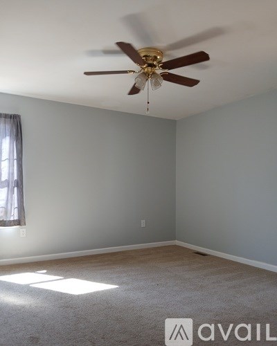 A room with a ceiling fan and a window letting in sunlight.