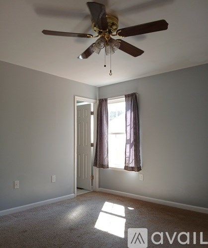 A room with a ceiling fan and a window with curtains.