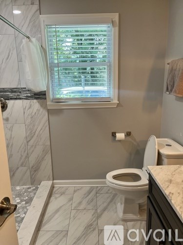 A bathroom with a toilet, a window with blinds, and a marble floor.