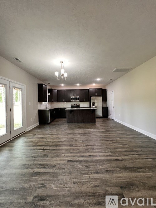A spacious kitchen and living room with dark wood flooring and white walls.