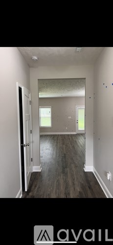 A room with wooden flooring and white walls, with a door on the left and a window on the right.