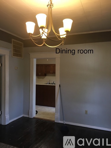 A dining room with a chandelier and a kitchen in the background.