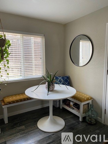 A round white table with a plant on it sits in a room with a window and a mirror on the wall.