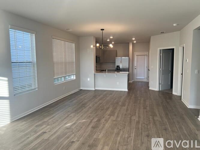 A spacious room with wooden flooring and a kitchen area in the background.