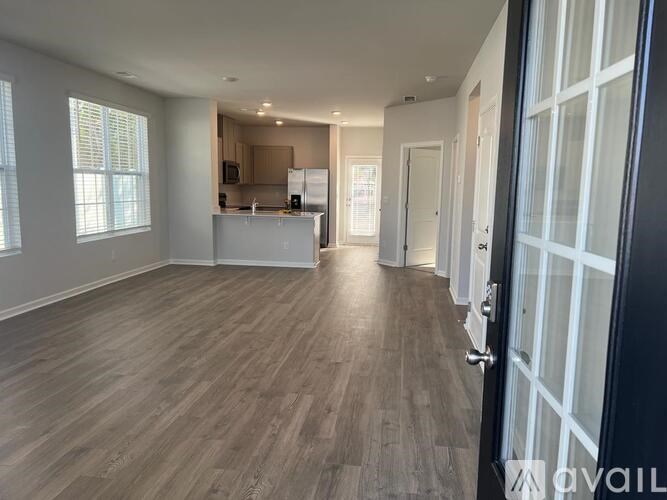 A spacious room with wooden flooring and a kitchen area in the background.