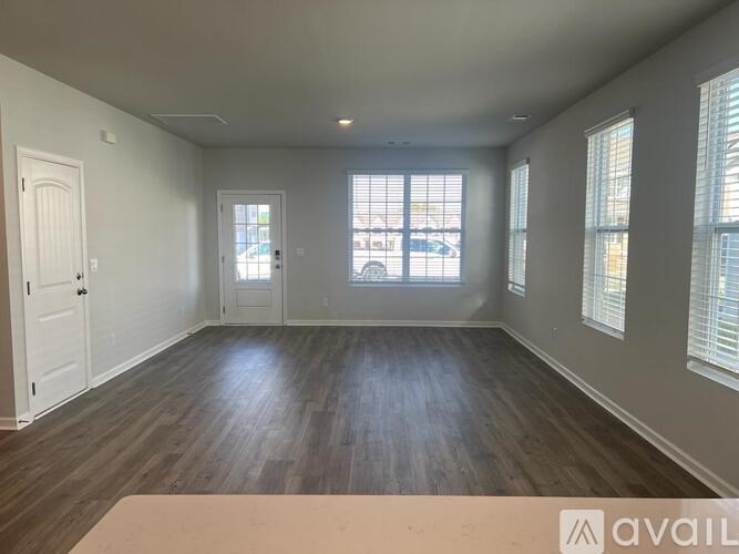 A room with wooden floors and white walls, with a large window and a door.