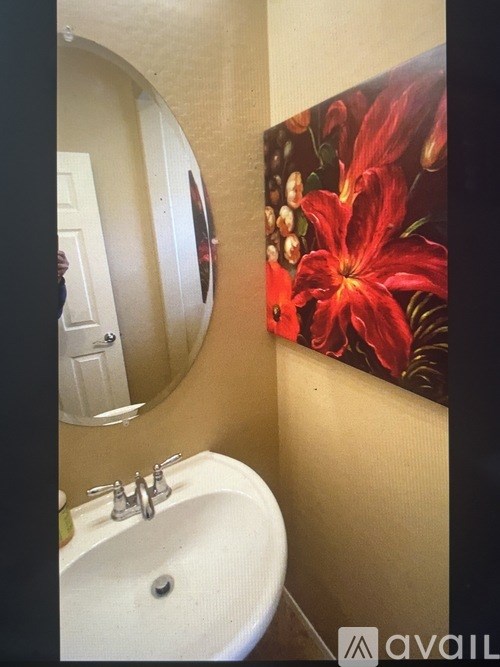 A bathroom with a white sink and a painting of red flowers on the wall.