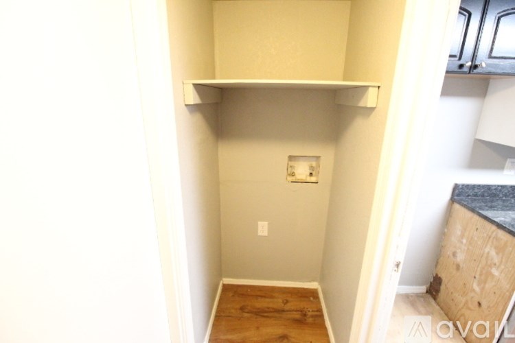 A small, empty room with a wooden floor and a light switch on the wall.