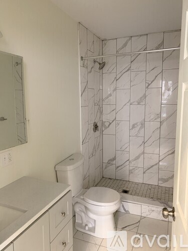 A white toilet sits in a bathroom with a marble tile shower.