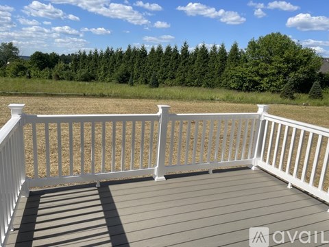 A deck with white railings and a wooden floor overlooks a grassy field.