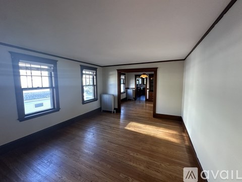 A room with wooden floors and white walls, with a window on the left side.