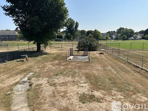 A large, open, grassy field with a tree and a fence.