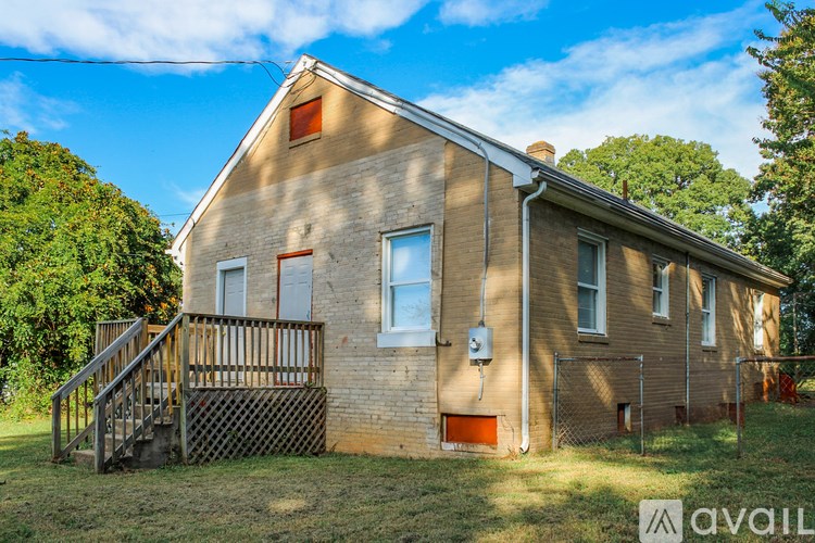 A house with a brown brick exterior and a red door is surrounded by a grassy area and trees.