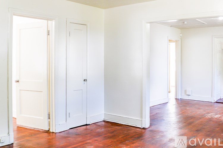 A room with white walls and wood floors, with three doors and one window.