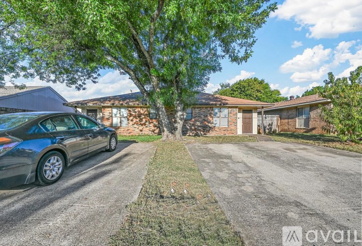 A blue car is parked on the left side of a driveway leading to a house.