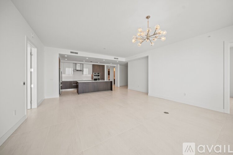 A spacious living room with a chandelier and a kitchen in the background.