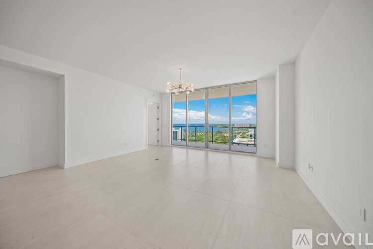 A spacious room with a chandelier and a view of the outside through the windows.