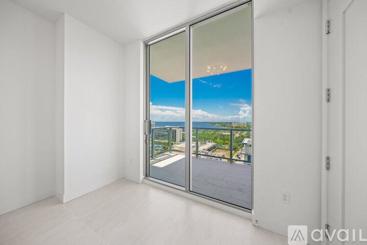 A room with a sliding glass door that opens to a balcony with a view of the city.