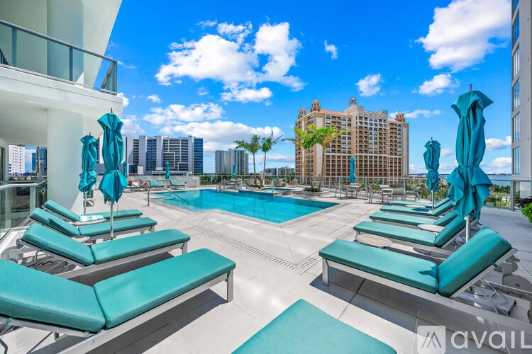 A pool area with sun loungers and umbrellas in front of a city skyline.