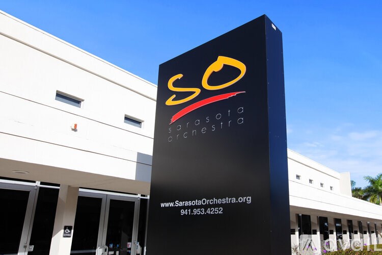 A tall black sign with the letters SO on it in front of a building.