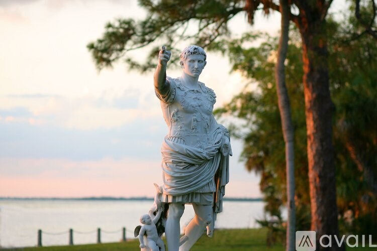 A statue of a person in a dress is in the foreground with a body of water and trees in the background.