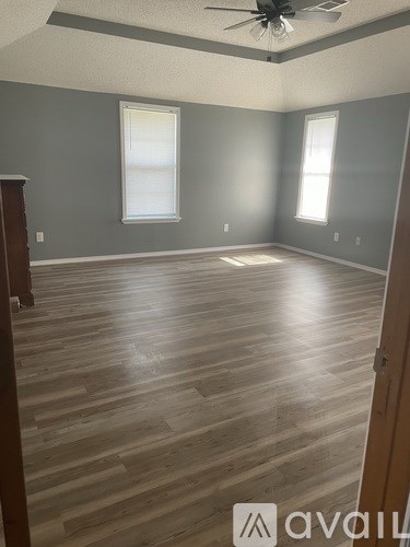 A room with wooden flooring and two windows.