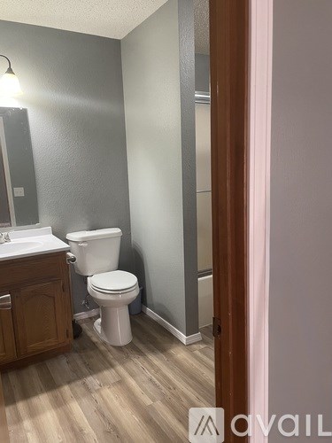A white toilet sits in a bathroom with wood floors and grey walls.