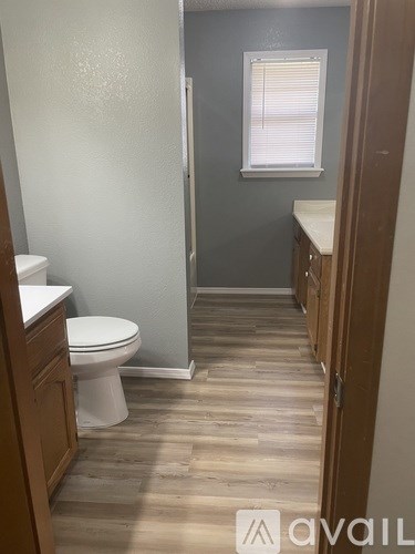 A bathroom with a toilet, wooden floors, and a window with blinds.