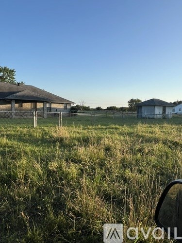A grassy field with a building and a fence in the distance.