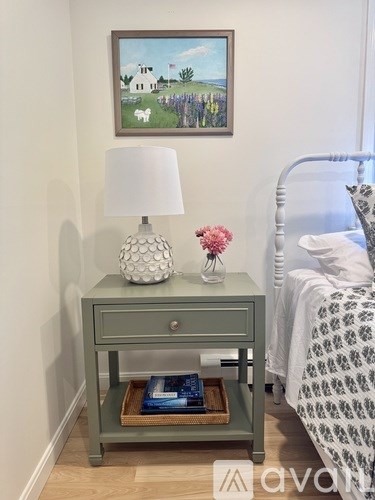 A bedroom with a bed, nightstand, and a painting on the wall.