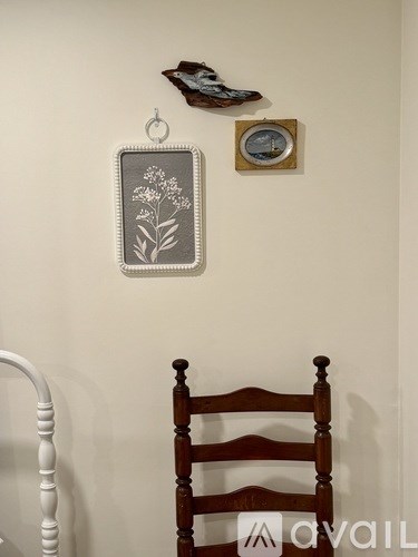 A wooden chair is in front of a wall with a clock and a picture frame hanging on it.