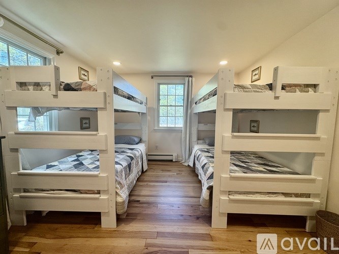 A room with white bunk beds and wooden floors.