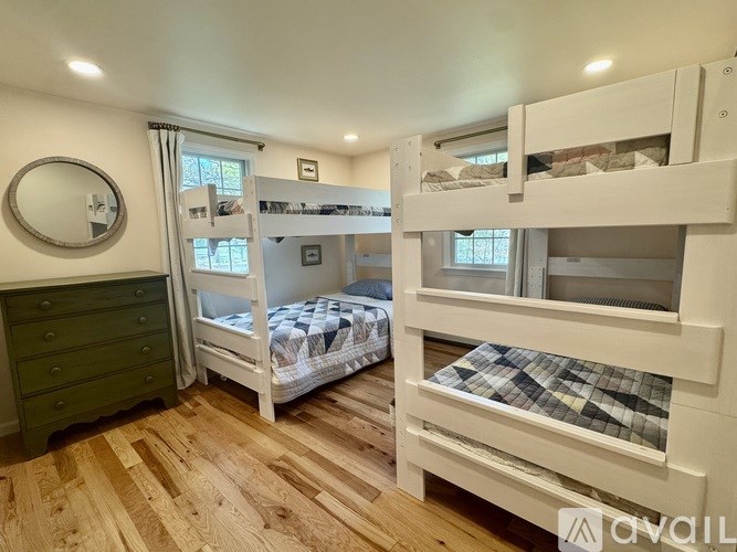A room with wooden floors and white walls has two bunk beds and a green dresser.