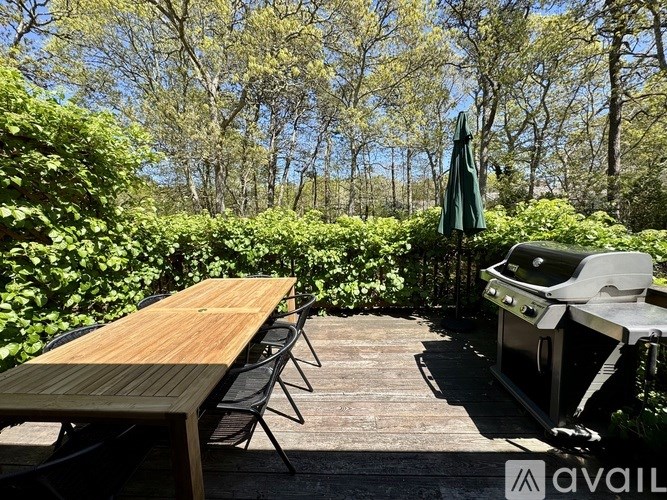 A wooden table is set up on a wooden deck with a grill and chairs.