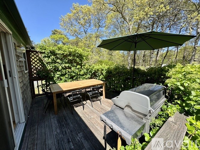 A wooden table is on a deck with a grill and umbrella.