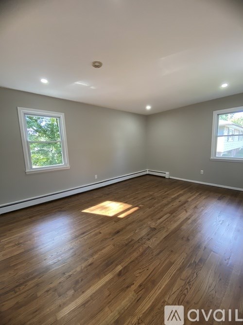 A room with wooden flooring and two windows.