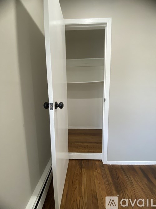 A white door with a black handle is open to a room with a wooden floor.