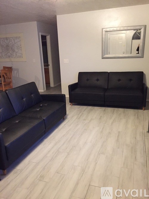 Two black leather sofas in a room with wooden flooring and white walls.