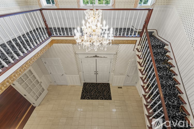 A chandelier hangs from the ceiling of a staircase with a black and white runner.