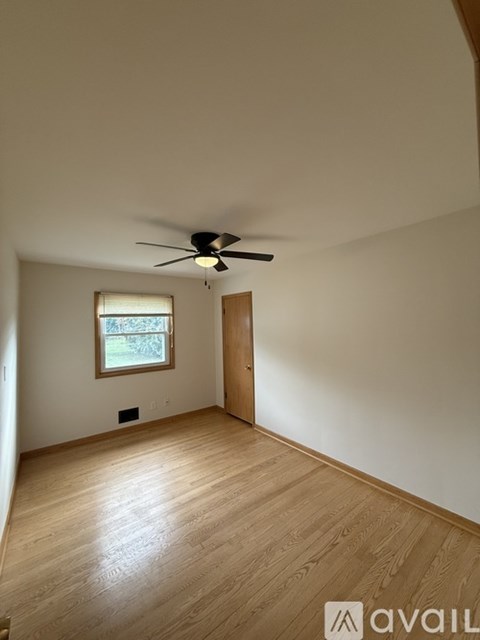 A room with a ceiling fan and a window with a view of trees.