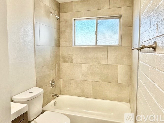 A bathroom with a tub, toilet, and a window.