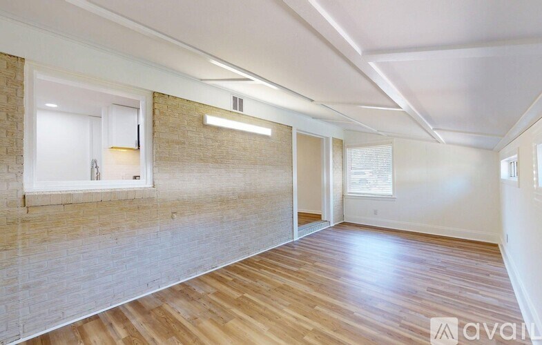 A spacious room with wooden flooring and a window with blinds.