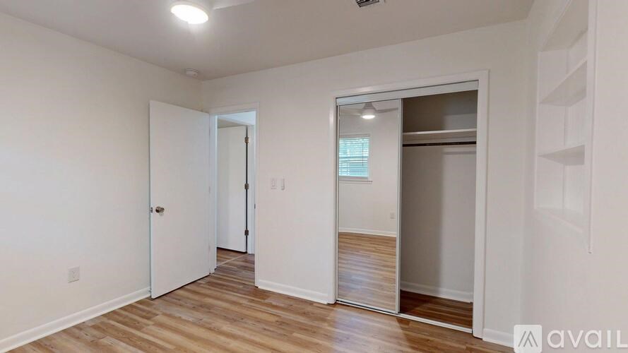 A room with wooden floors and white walls, with a door on the left and a closet on the right.