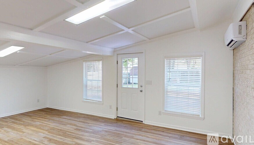 A room with a white ceiling, wooden floor, and a white door.